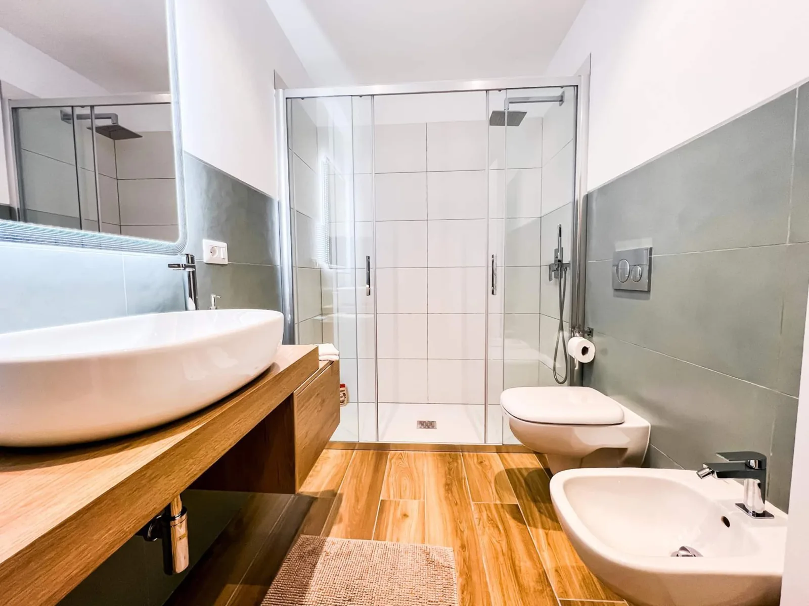 Il bagno con doccia a vetro, lavabo d'appoggio sul piano in legno e bidet
