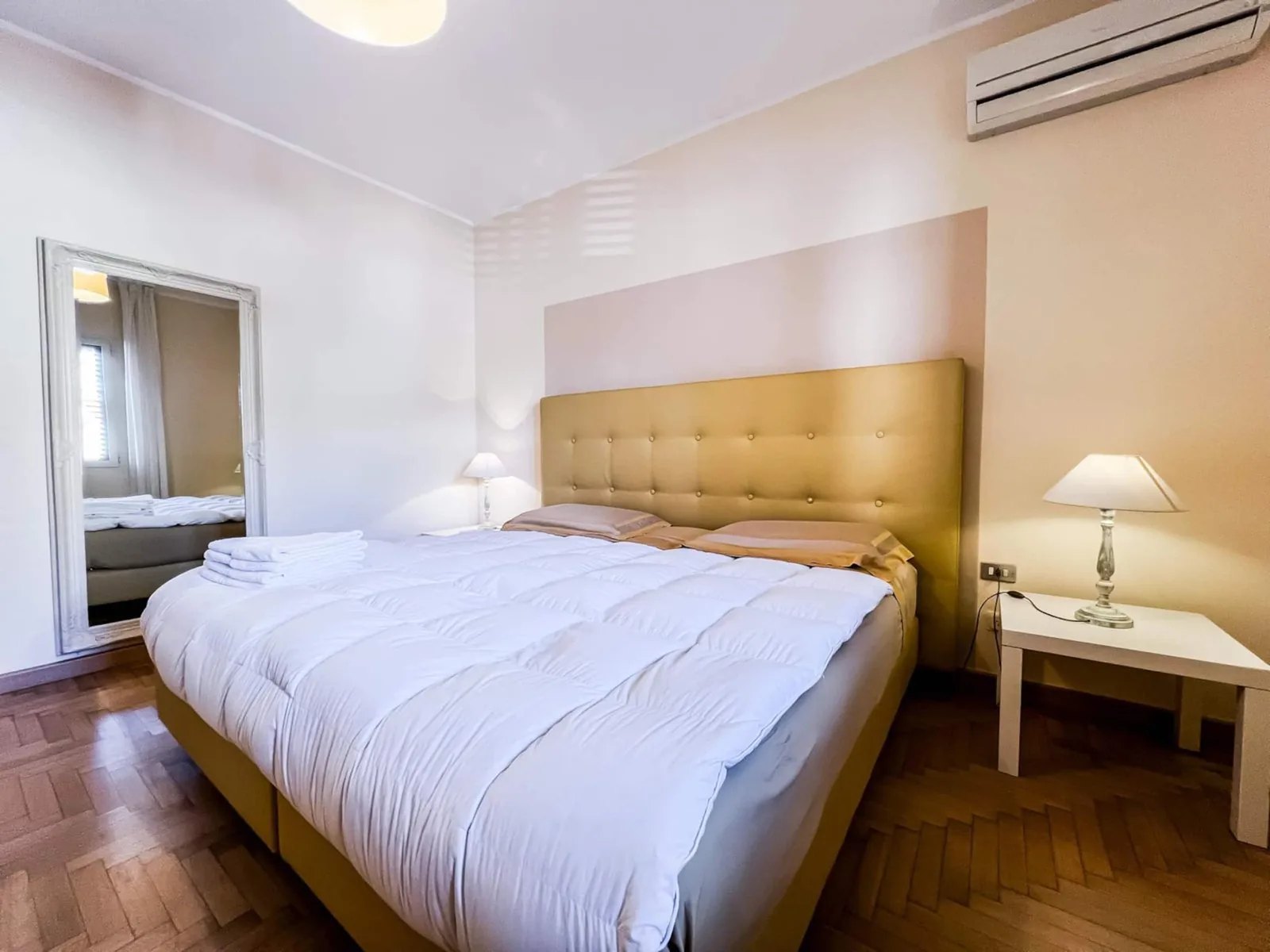 Camera matrimoniale con climatizzatore a parete, specchio grande e lampada sul comodino
