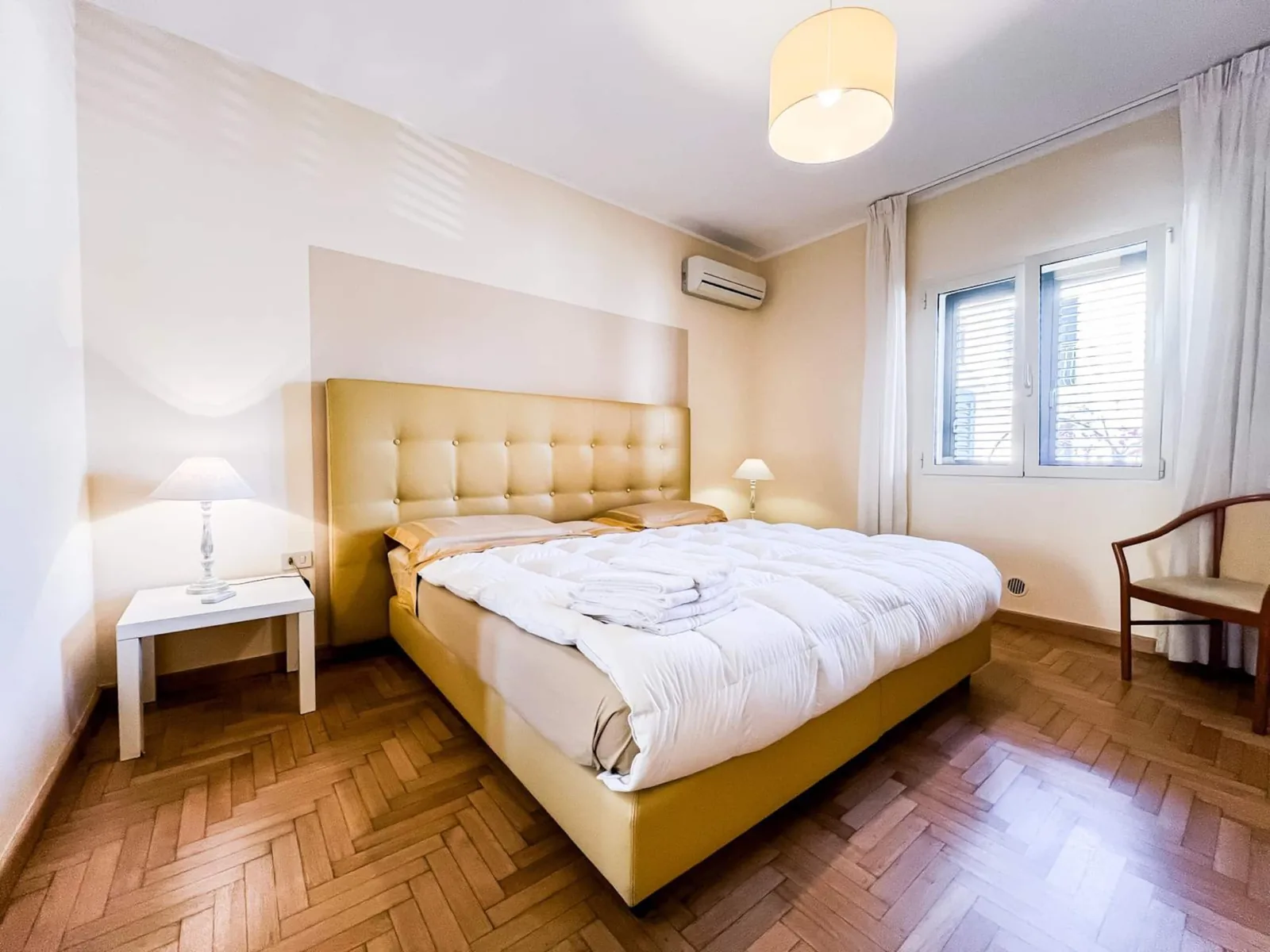 Camera matrimoniale con testiera imbottita, comodini bianchi, lampade e finestra sul lato interno